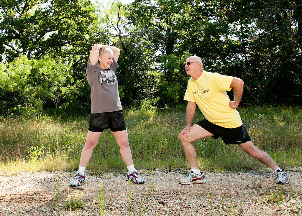 Two senior adults stretching on a path