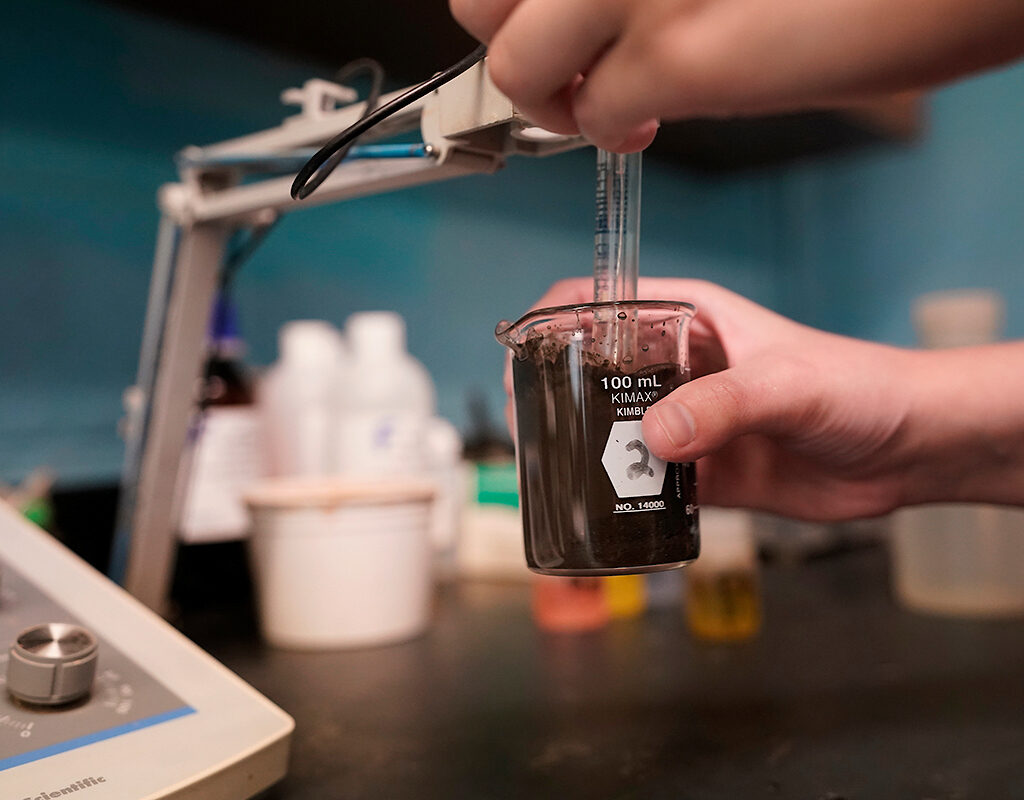 Hands testing a soil sample in a beaker