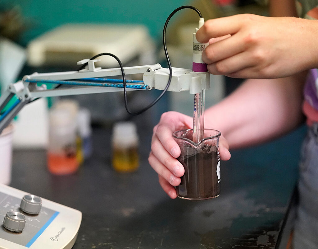 Hands testing a soil sample in a beaker