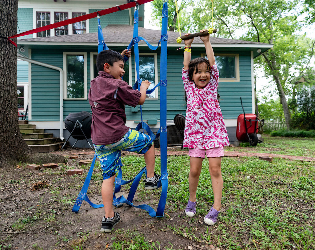 Two children play on a slack line outside a house
