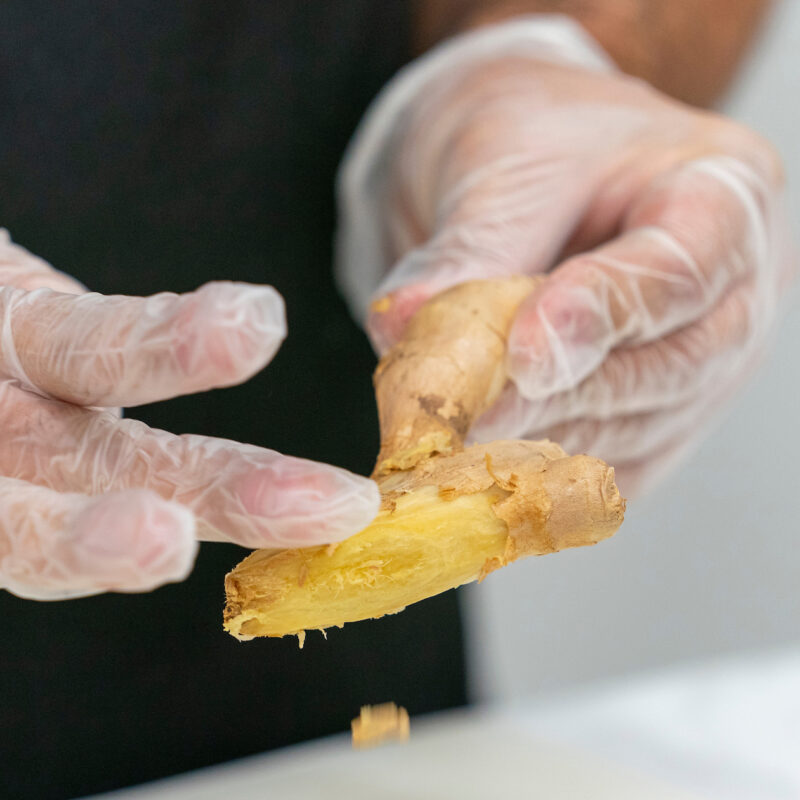 gloved hands peeling a ginger root